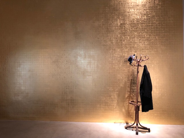 A hat and coat on a coat rack against a bare gold leaf wall 