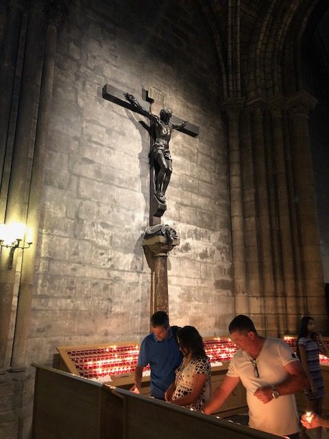 Crucifix on the wall, with people lighting candles beneath it 
