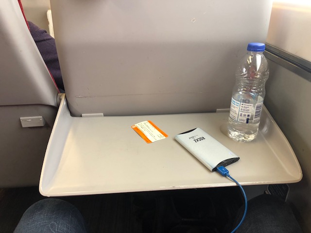 Train ticket, portable charger, bottle of water on the pull down tray 