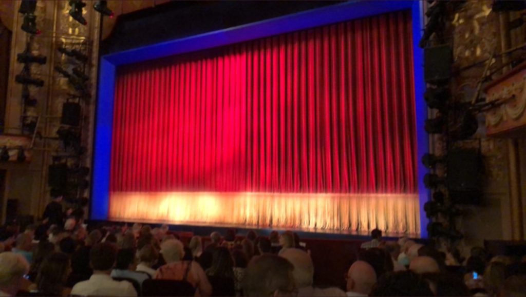 The stage: red curtain with a cream colored band along the bottom, maybe 3 feet high. Stage framed in blue light.