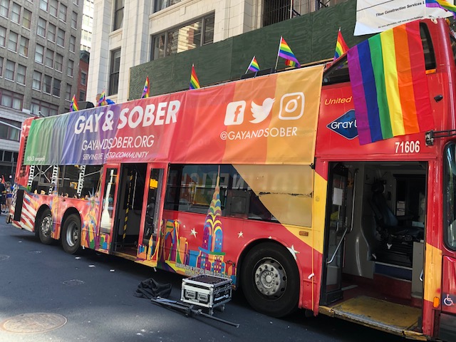 Huge Gay & Sober banner in rainbow colors on the side of the bus running the full length