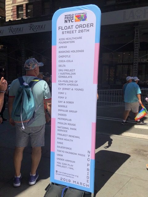 A sign on the street indicating all of the companies whose floats were staged on 26th, including Chipotle, Google, Indeed, Salesforce, and Uber