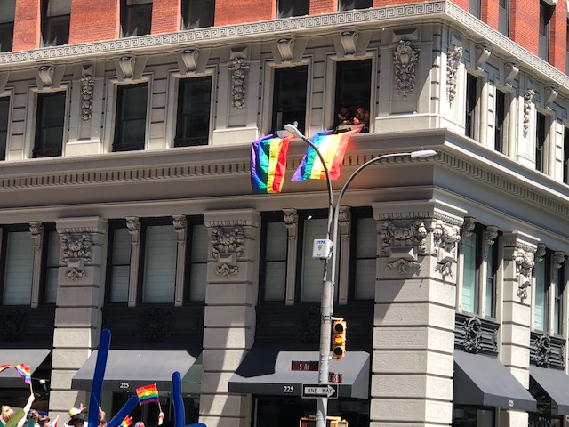Rainbow flags draped from 2 windows on the 2nd floor of a building at the start, people watching from there