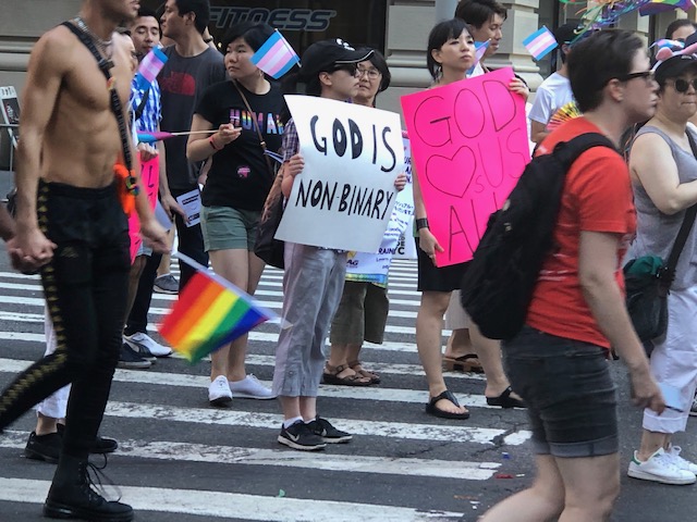 Chinese woman carrying a sign that says "God is non binary"