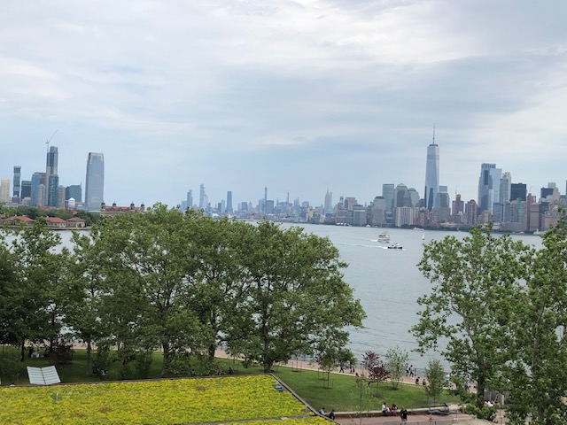 Jersey City and NYC in the background, trees and grass in the foreground from the park