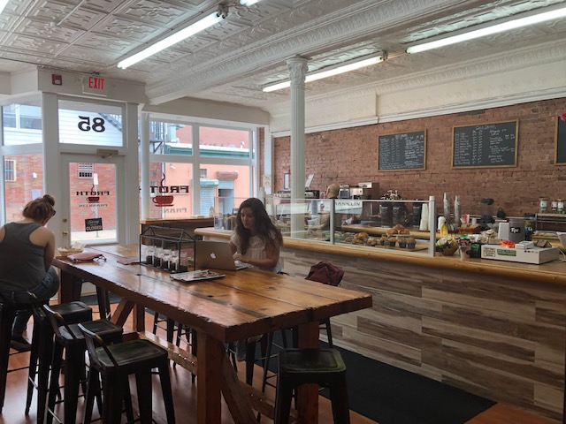 The main area of the cafe: a communal table in the middle seating about 8, the counter and cashier in the background, front door to the far left