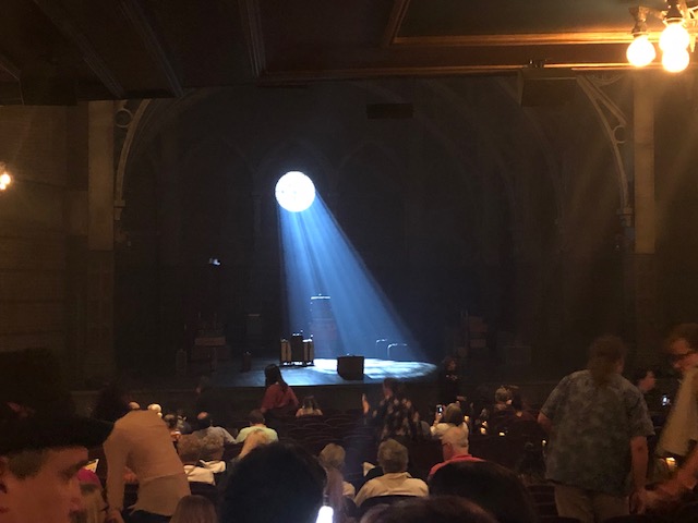 A beam of light form a perfect circle in the back wall streaming down onto the stage