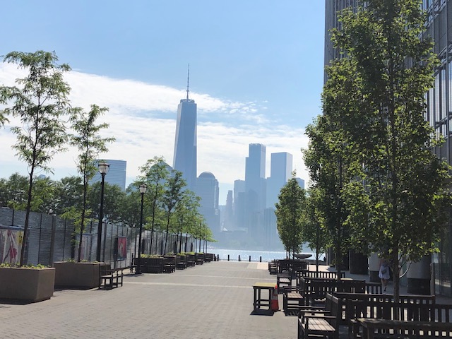 World Trade Center from Jersey City, framed by a tree lined walkway, and a tall buildin on the right
