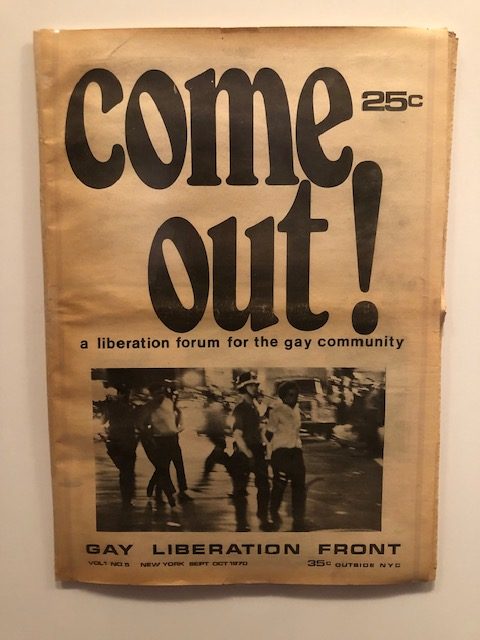 An old pamphlet of the Gay Liberation Front, with "come out" on the cover taking up half of it, with a photo underneath of policy taking people away in handcuffs