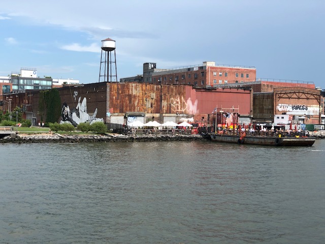 A bar on the river bank, at the end of the building the mural is on, which extends onto a barge on the water