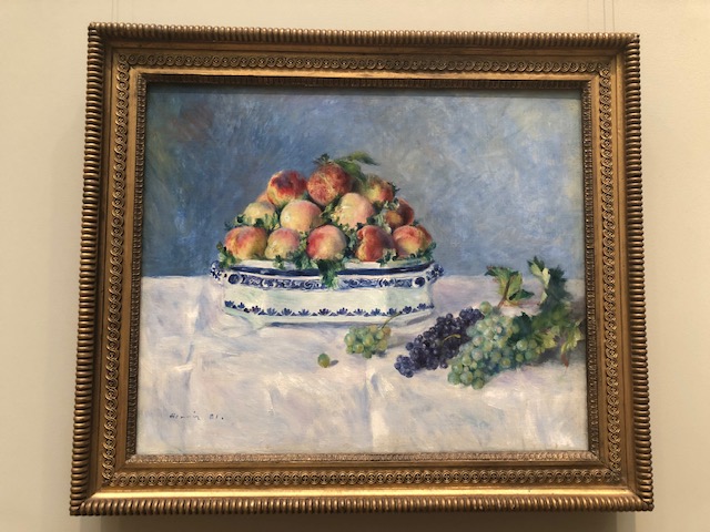 peaches in a white bowl with decorative blue trim, purple and green grapes lieing being is on a white tablecloth