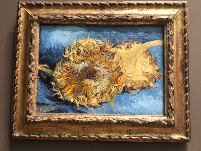 A huge sunflower facing you, takes up almost 2/3 of the canvas, with another upside down behind it