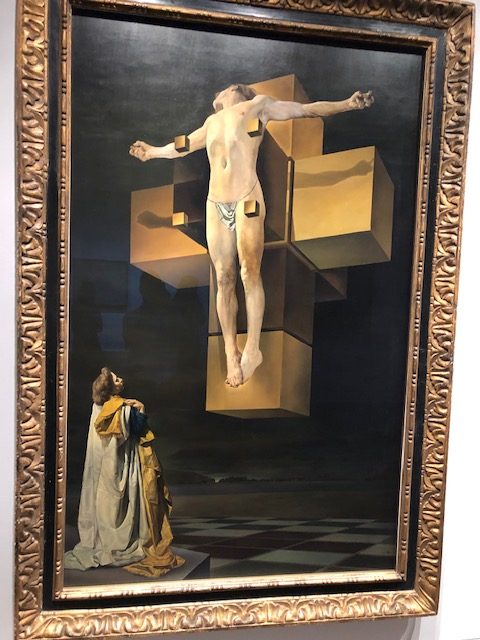 A healthy looking but naked Christ levitating in front of a cross that's cube-line in form