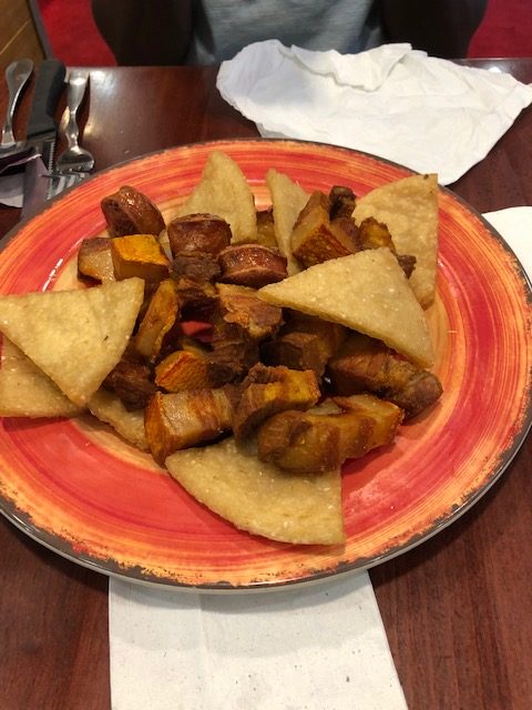 A red clay plate willed with fried bite sized meat and crispy triangles of corn meal