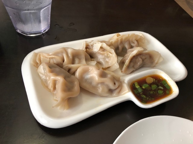 A plate of dumplings with a little side bowl hewn into the plate, with soy sauce and green onions