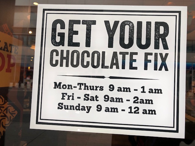A sign with Get Your Chocolate Fix in the top half, store hours in the bottom half