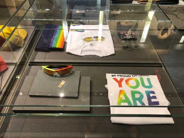 Glass display with Pride t-shirt "be proud of who you are" in rainbow colors, rainbow sunglasses