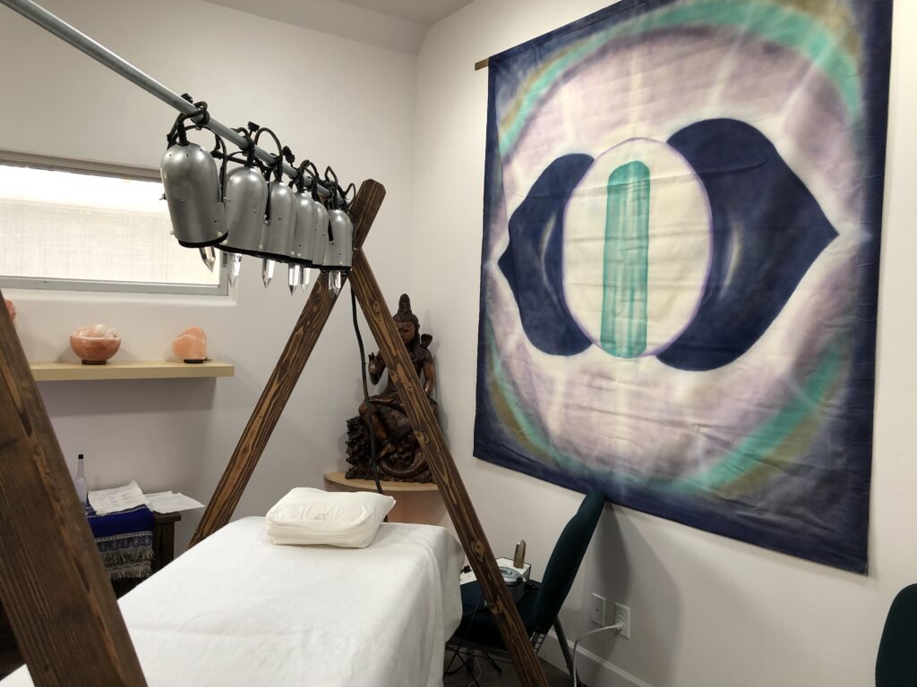 what looks like a massage table, but in a wooden frame with high posts like a tee pee on each end. There's a bar resting in the cross sections at the top, and lights hanging down from the bar. There's a new age tapesty on the wall in blues, greens, white and yellow