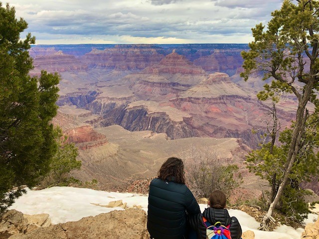 A mother and small child sitting on the canyon edge, framed by trees, canyon in the background