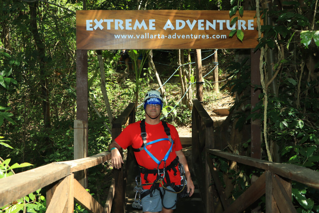 me standing below the Extreme Adventure sign, wearing all the gear for ziplining and rappelling 