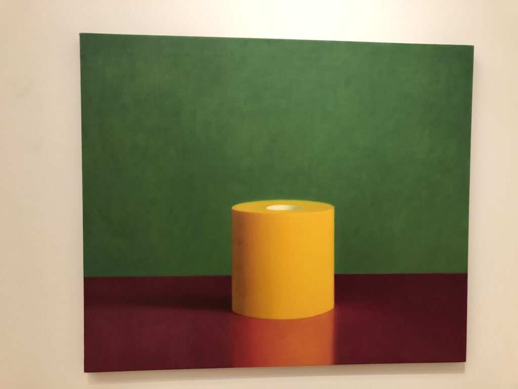 A yellow-orange roll of toilet paper against a green wall sitting on a red surface. 