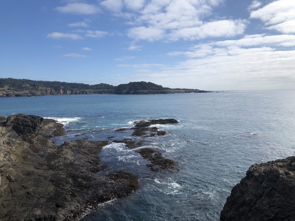 cliffs in the foreground, rocks in the middle, land in the background, ocean in the middle 