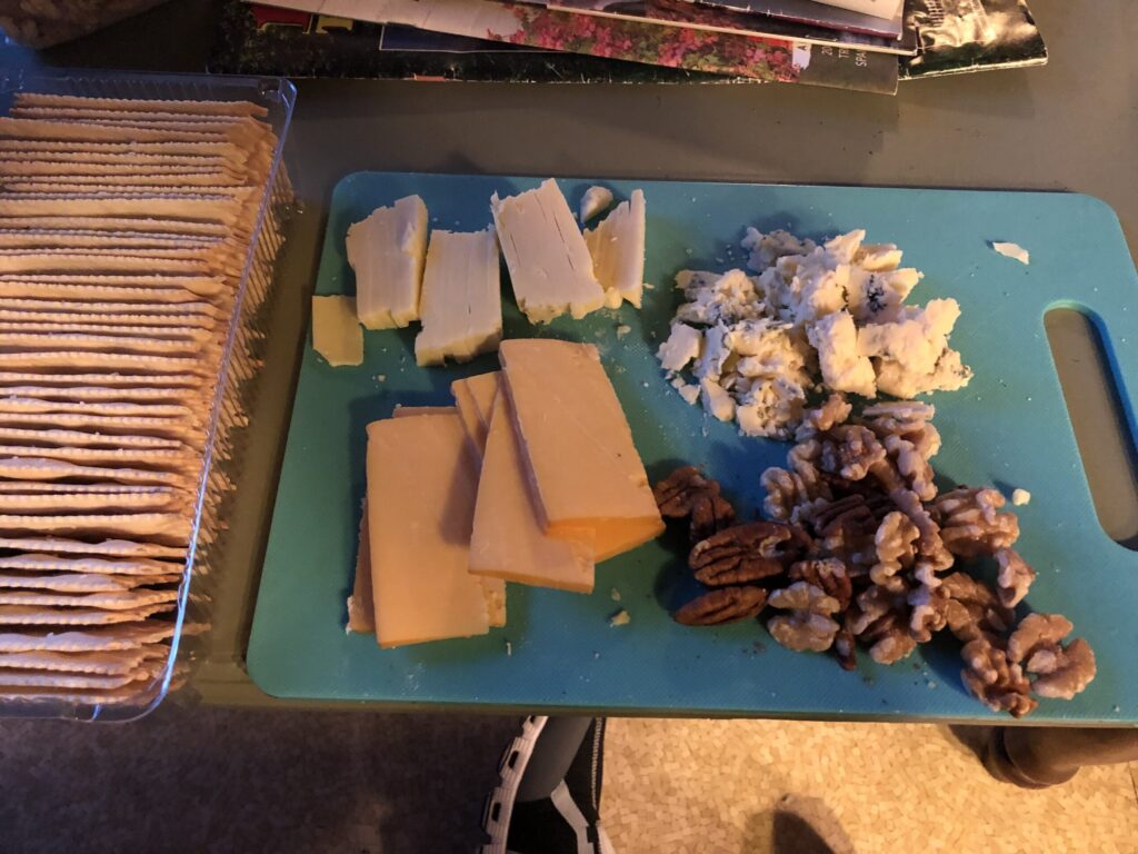 a tray of crackers on the left, with 3 kinds of cheese plus pecans on a cutting board 