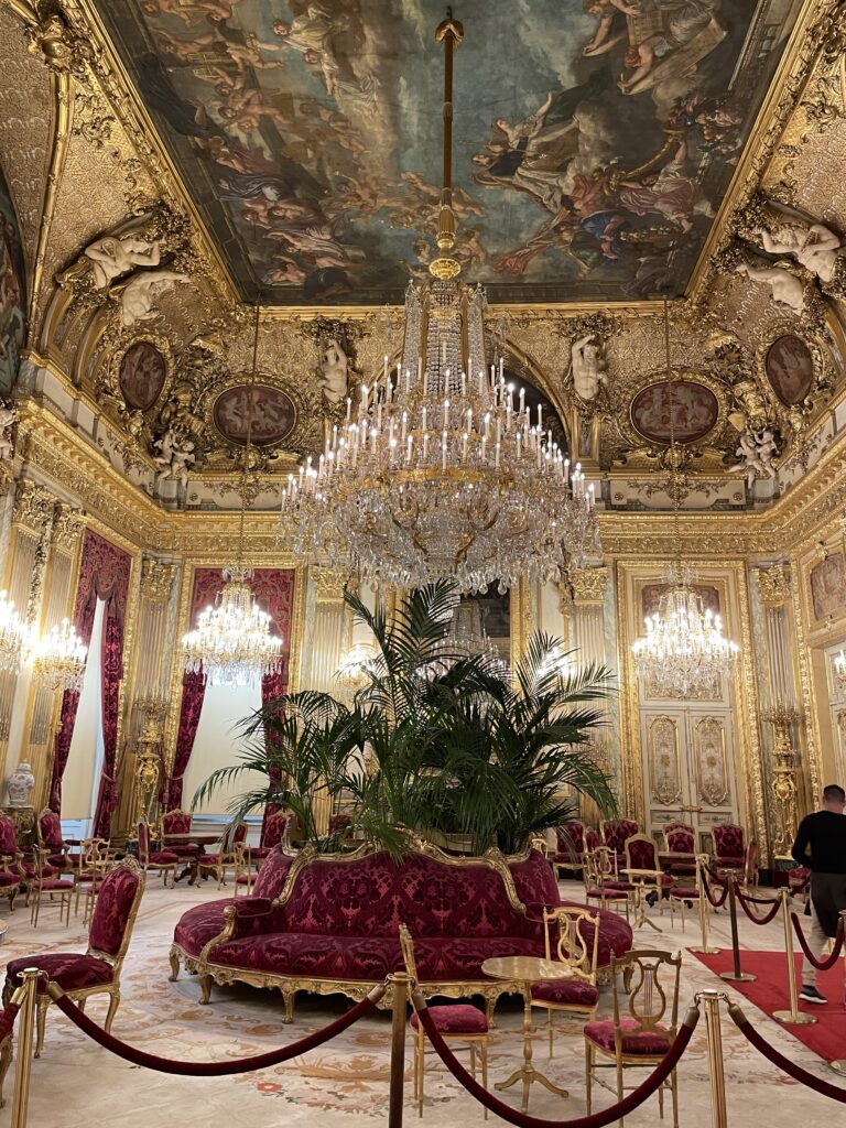 A spectacular room with sculptured gold walls, mural ceiling, red velvet circular couch, crystal chandeliers. 
