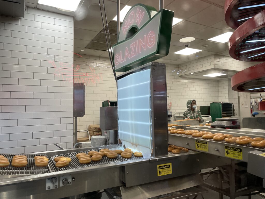 conveyor belts filled with donuts going through the glazing station 