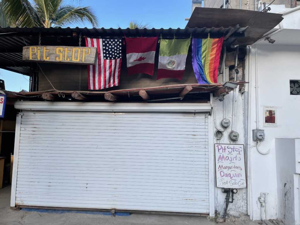 A closed shop with 4 flags hanging above the entrance: American, Canadian, Mexican, and LGBT. 